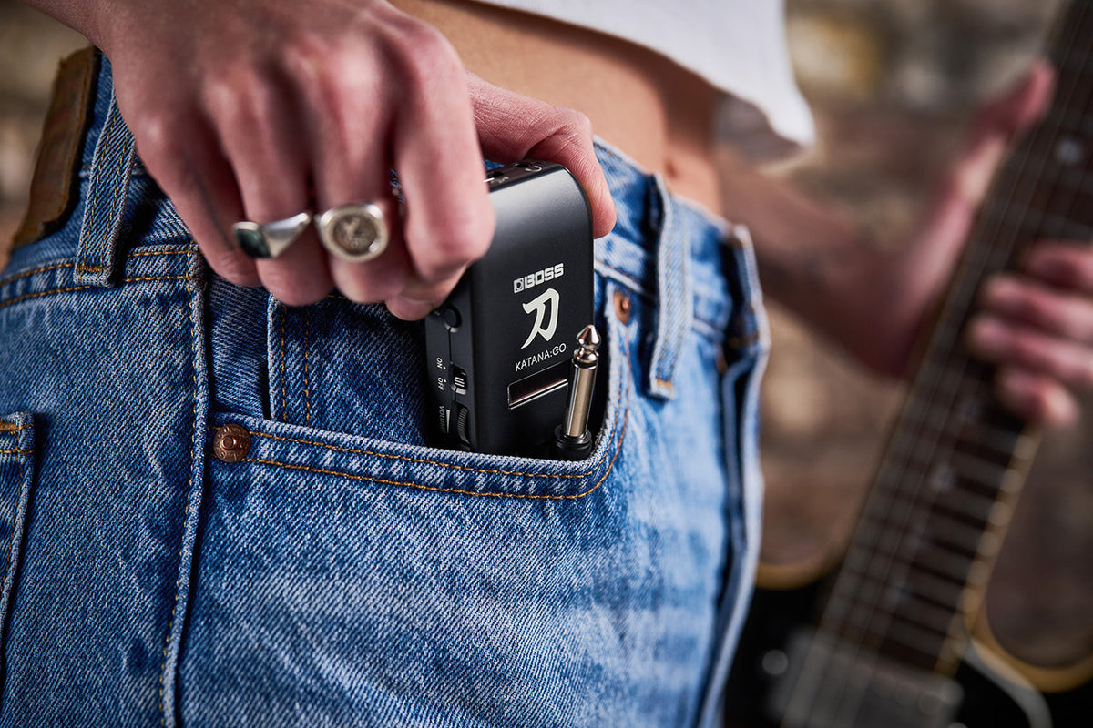 Boss Katana GO (KTNGO2) being slipped into a jeans pocket with the plug folded flat, showing how small the amp is