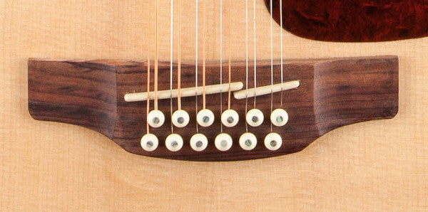 Split synthetic bone saddle on the laurel bridge of the Takamine GJ72CE-12 NAT, showing the two stepped saddle pieces that intonate the octave courses