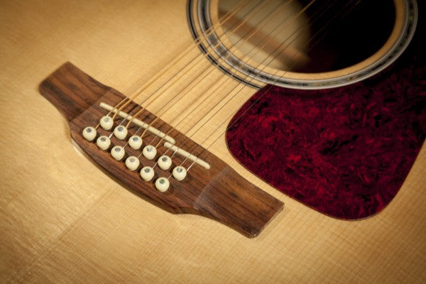 Laurel bridge with twelve bridge pins, abalone concentric rosette and burgundy pearloid pickguard on the Takamine GJ72CE-12 NAT
